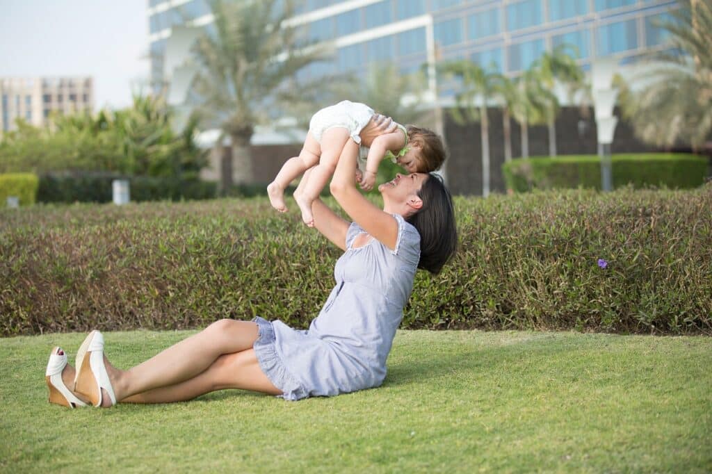 Mother holding her baby up in the air while sitting on a treated freshly mowed lawn in a park